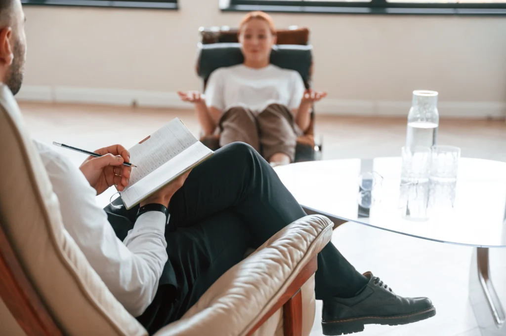 A therapy session where a woman reclines in a chair while a therapist takes notes.
