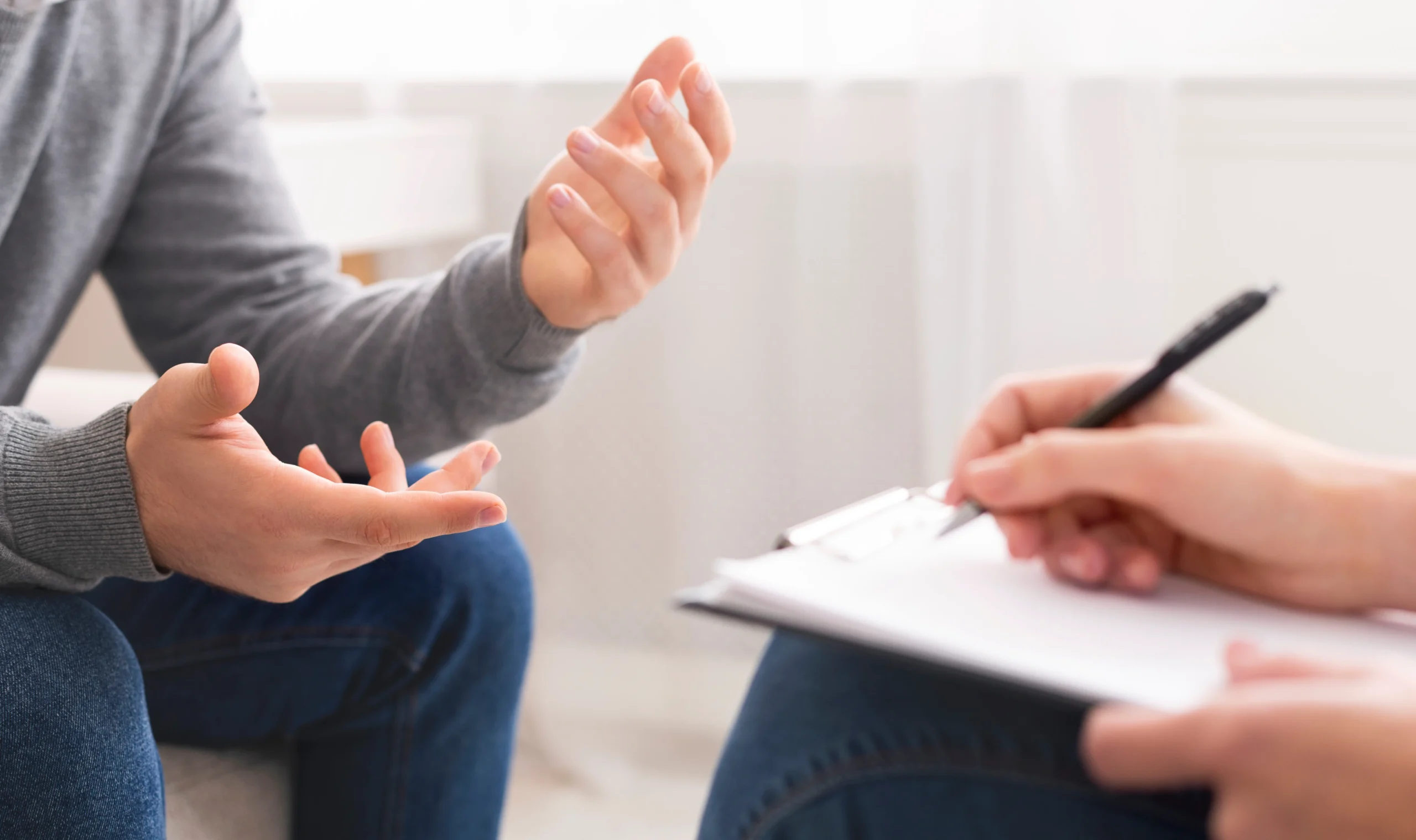 A close-up of a person gesturing with their hands while speaking to a therapist who is taking notes.