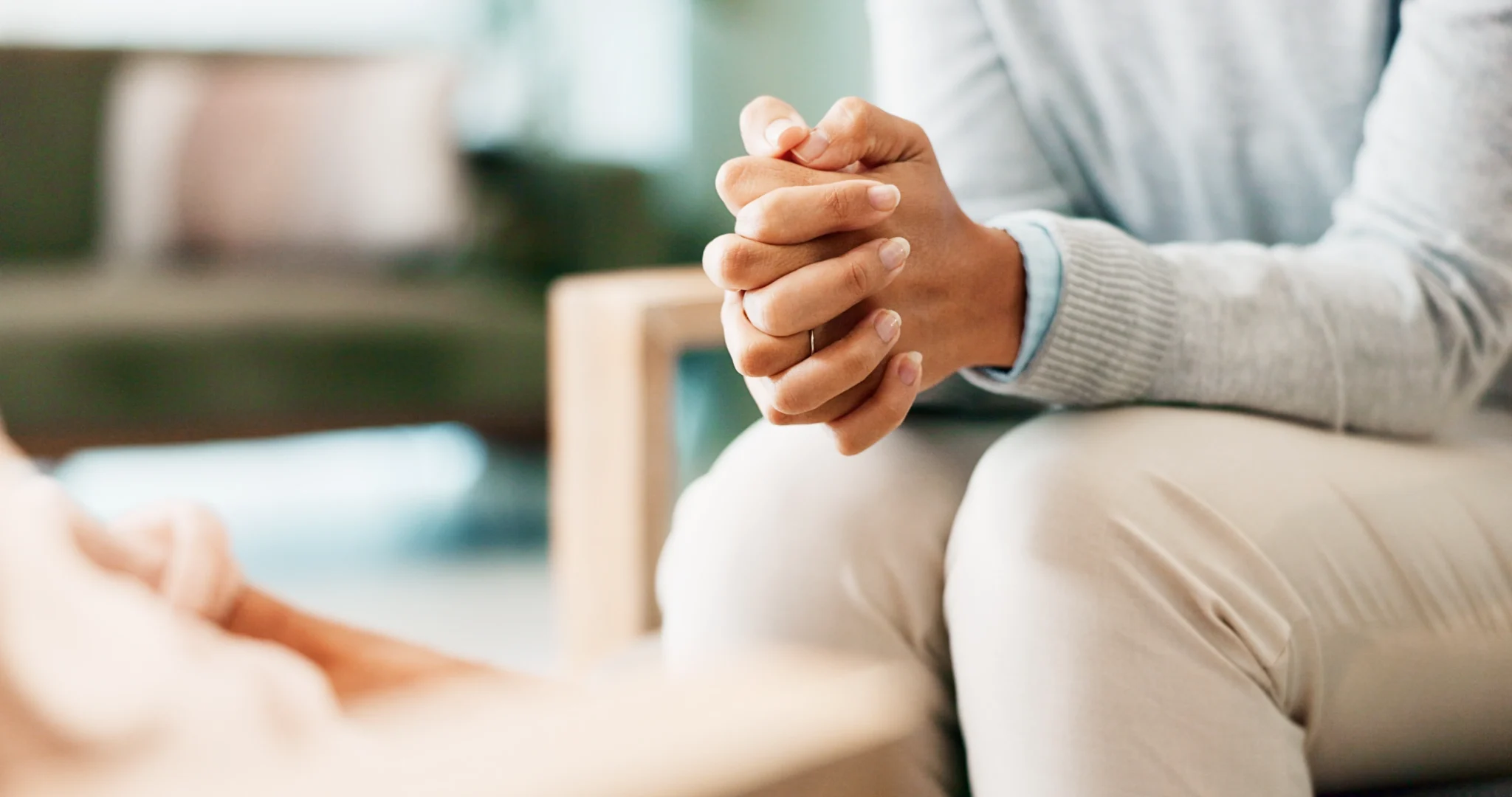 A close-up of a person's clasped hands in a therapy session, with a blurred background of a modern office.